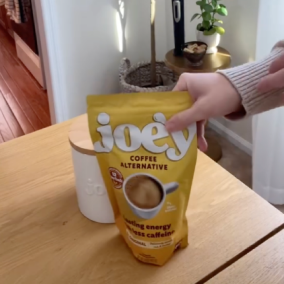 Person holding a bag of Joey coffee alternative on a wooden table.