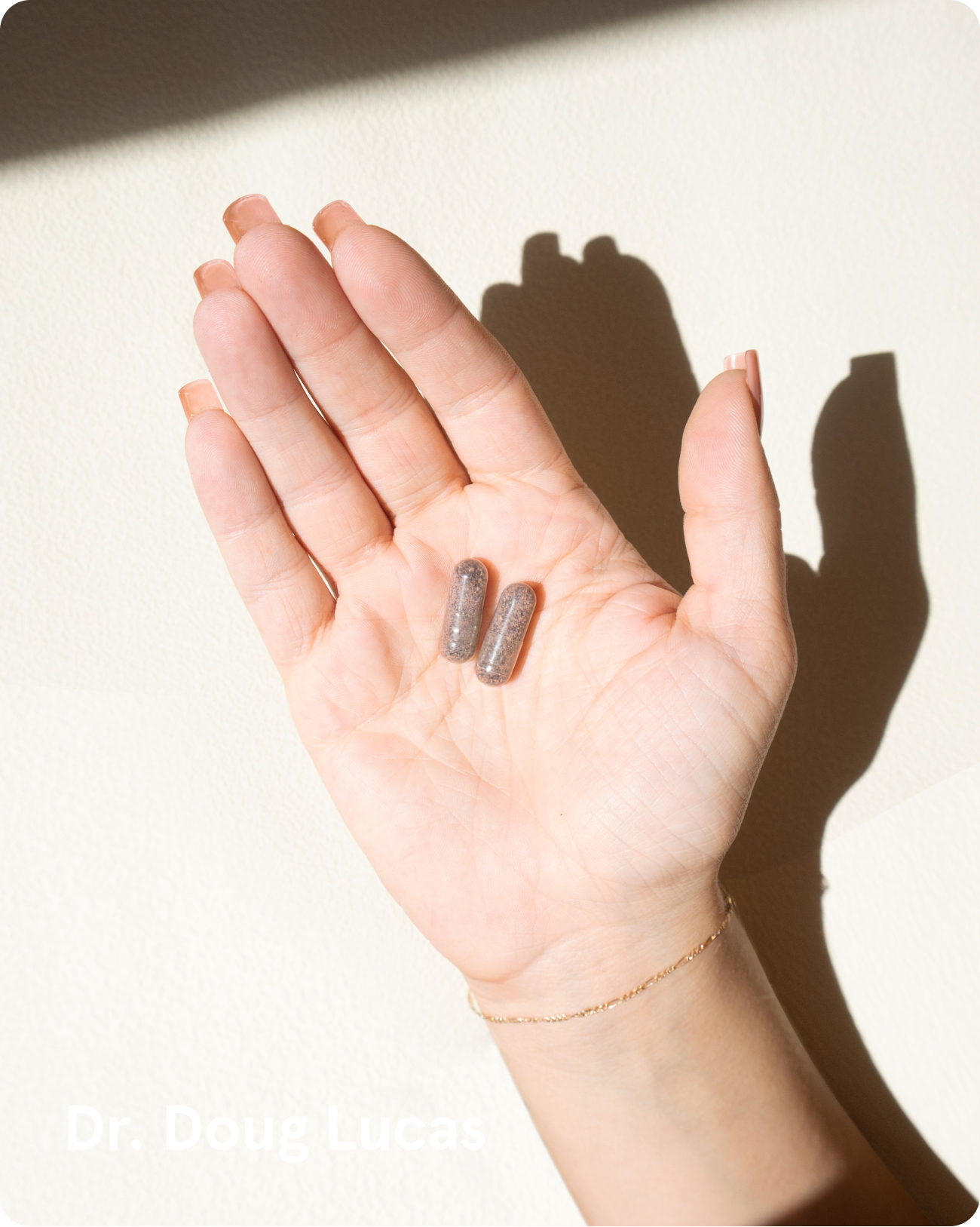 A person's hand with manicured nails holding two dark, speckled capsules in their palm.