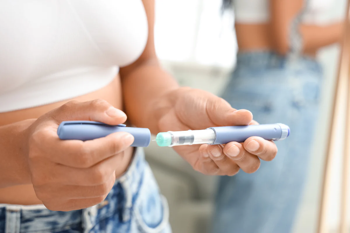 A close-up of a person's hands holding a blue insulin injector pen and removing the cap.