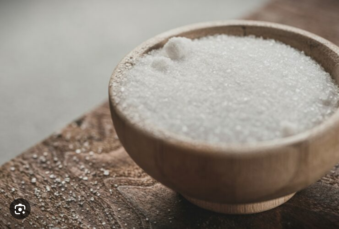 A wooden bowl filled with granulated white sugar on a rustic surface.