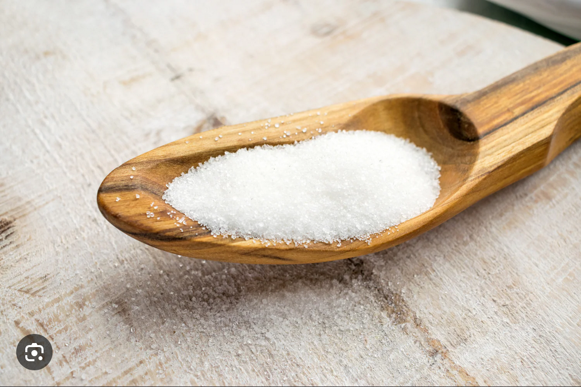 Wooden spoon with white granular substance on a wooden surface.