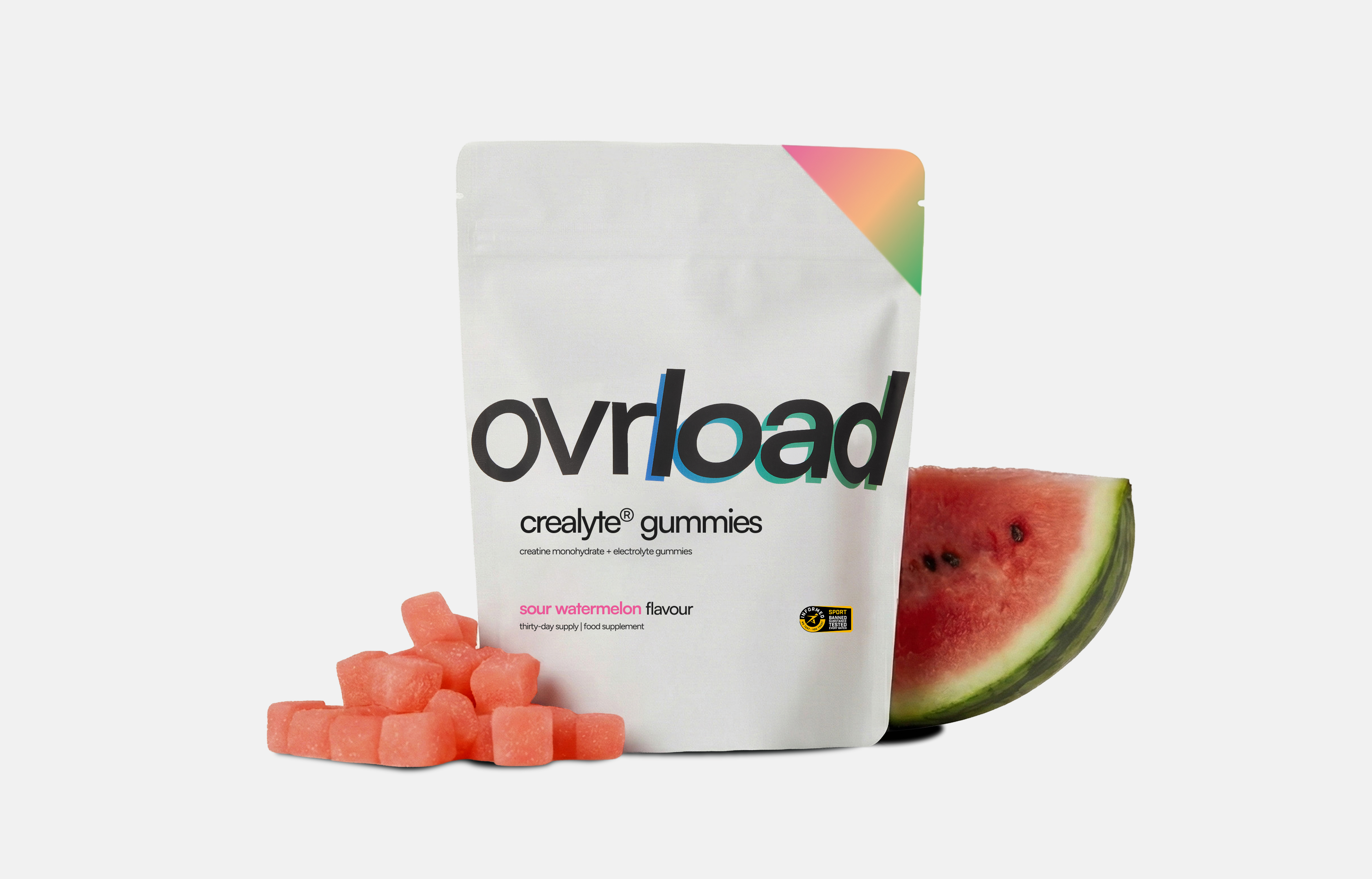 A pouch of Ovrload sour watermelon creatine gummies next to a pile of gummies and a watermelon slice.