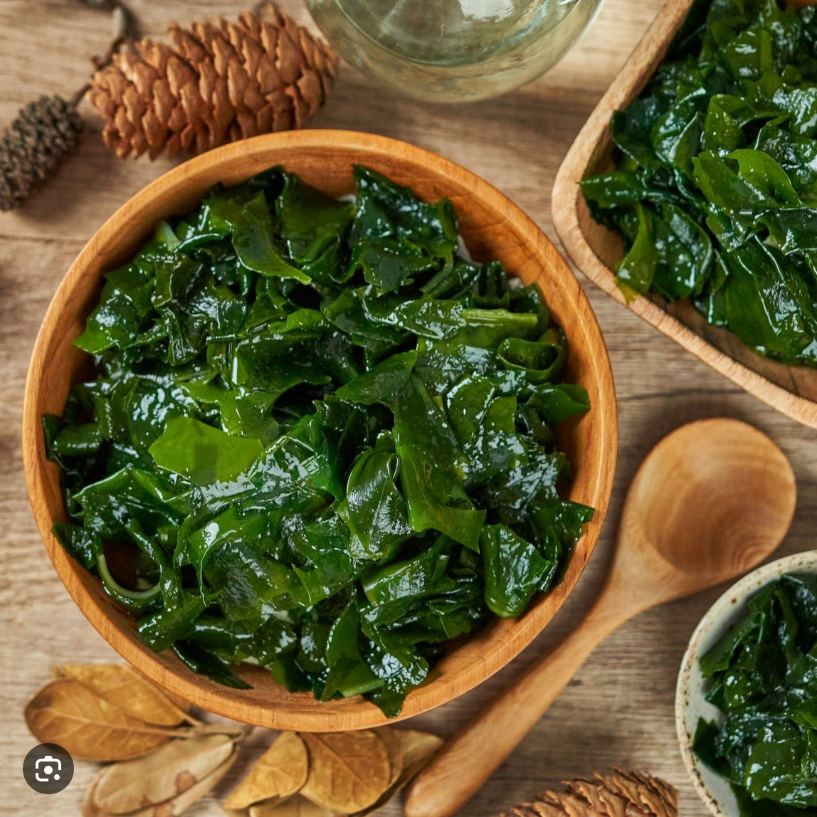 Bowls of green seaweed on a wooden table with pinecones and leaves.