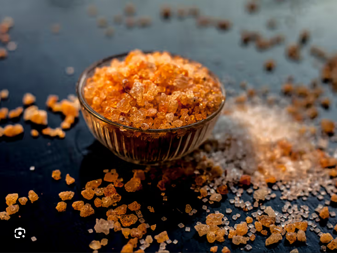 Glass bowl with orange crystals, scattered on dark surface.