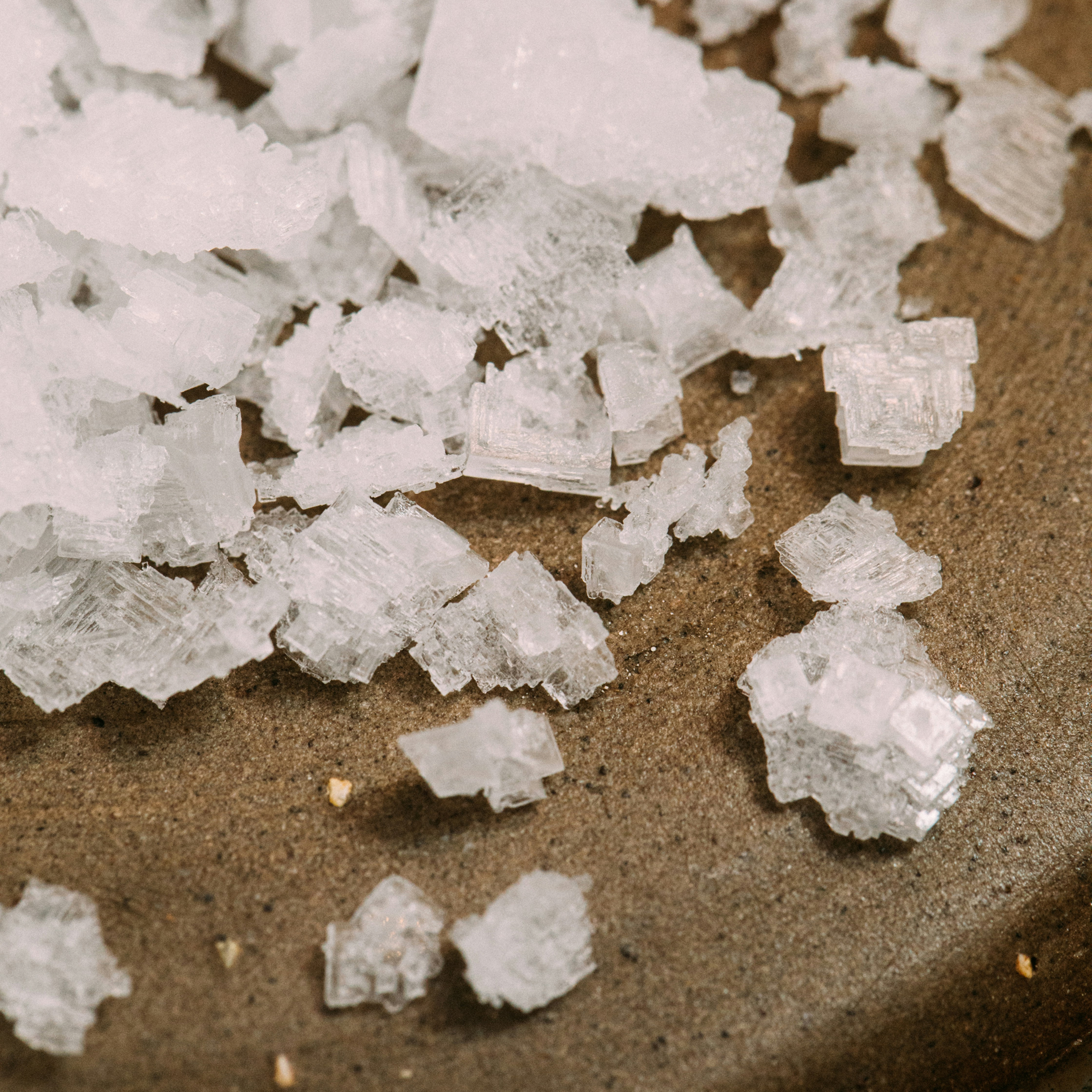 Close-up of coarse white salt crystals on a brown surface.