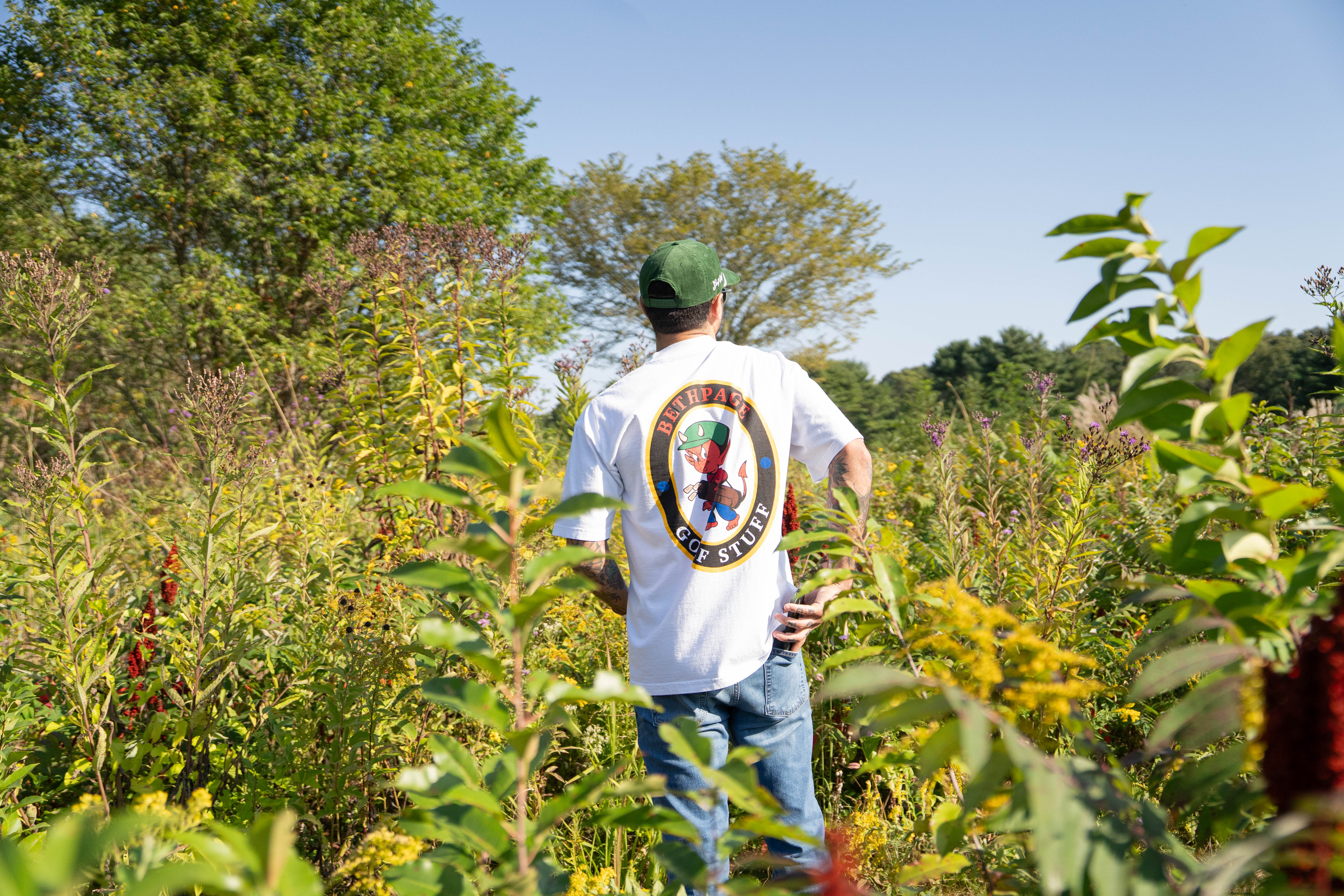 Person in field wearing a white graphic t-shirt and green cap.