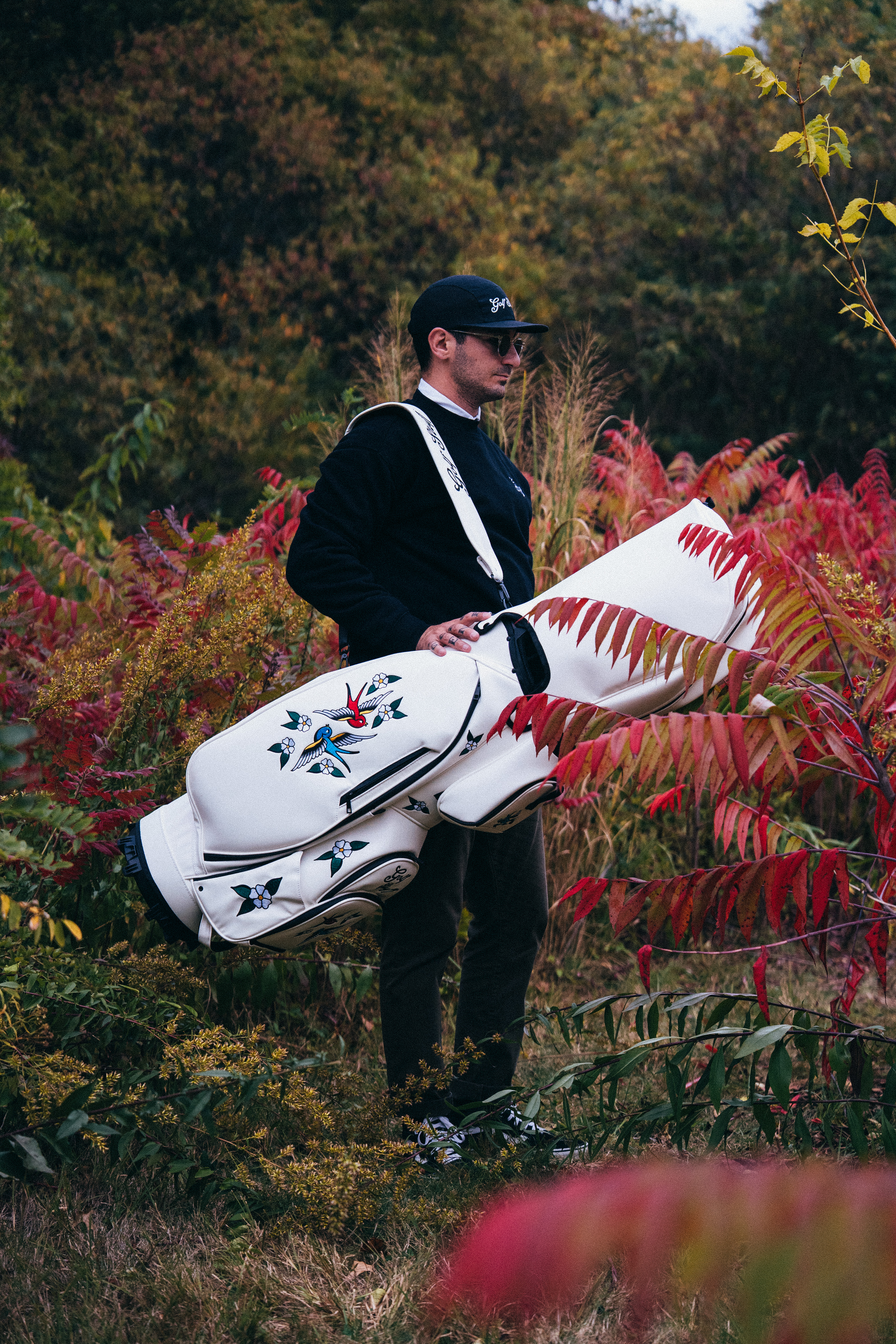 Person holding a decorated golf bag among colorful autumn foliage.