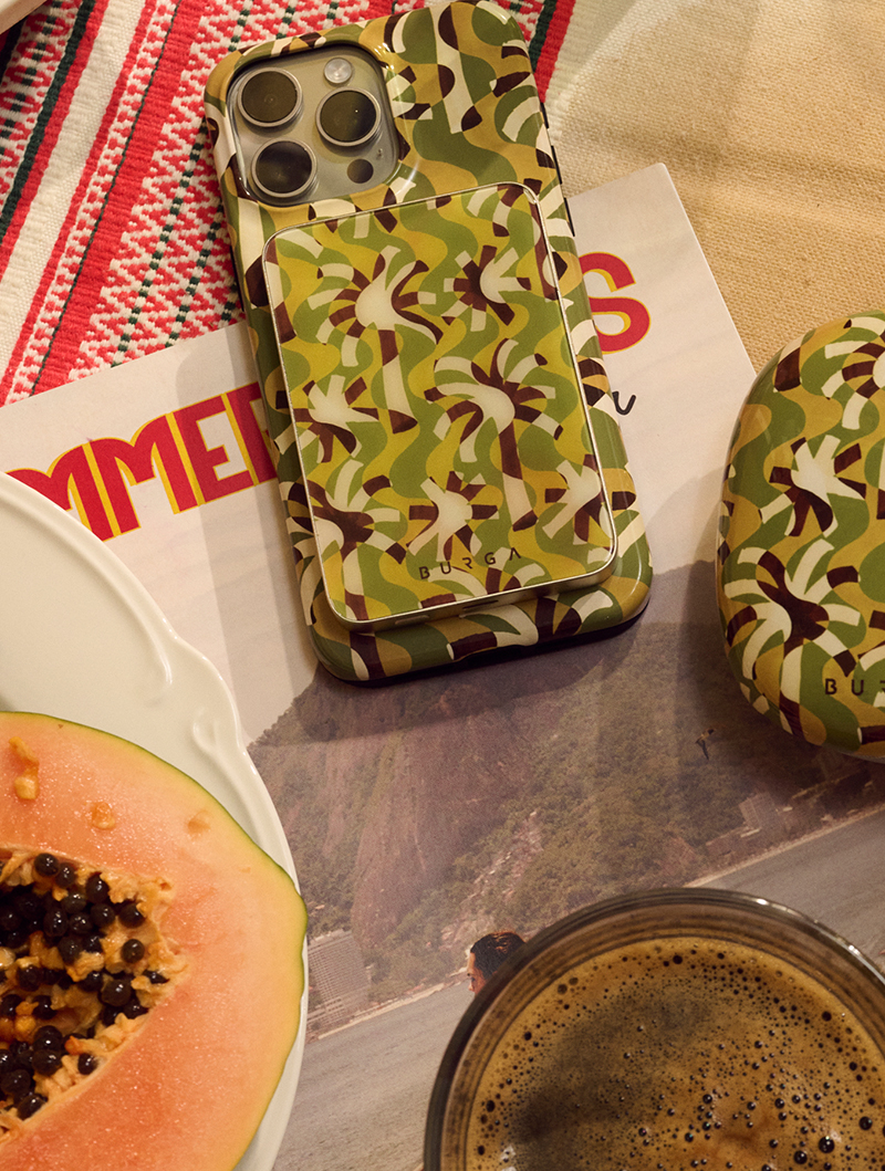 Phone with green patterned case on table with papaya and coffee.