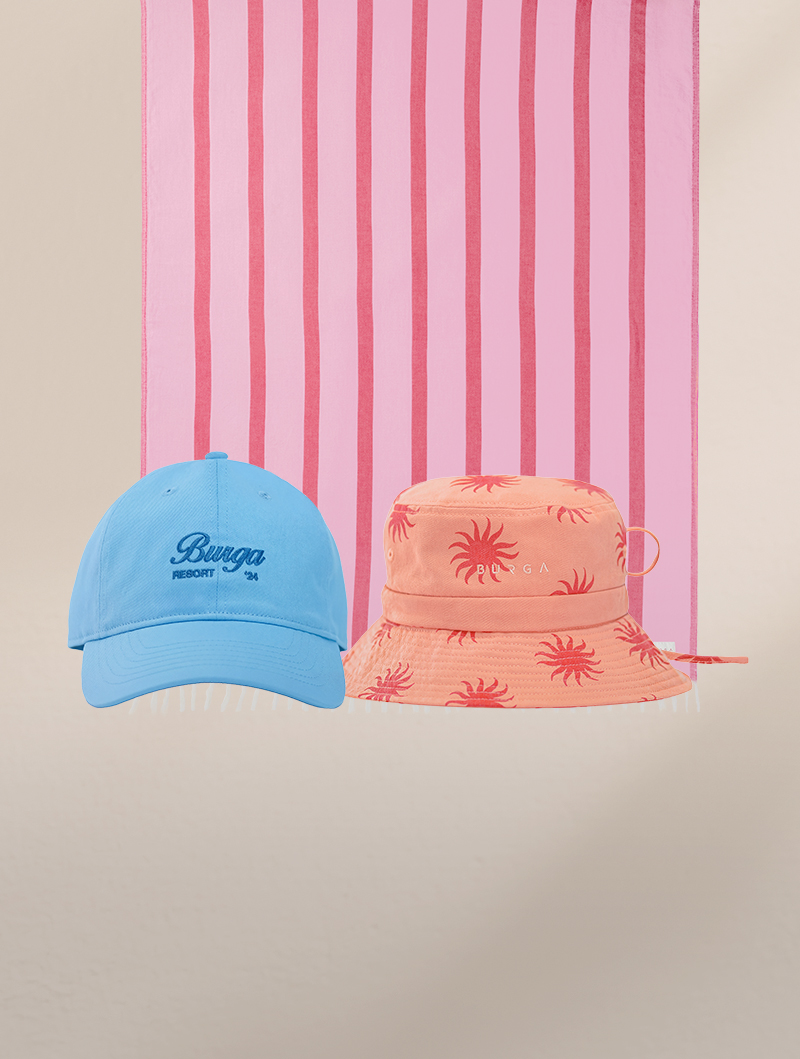 A blue baseball cap and a peach bucket hat sit in front of a pink striped towel.