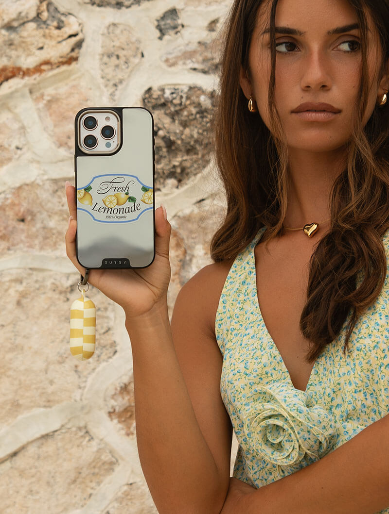 Woman holding a phone with 'Fresh Lemonade' case, standing against a stone wall.
