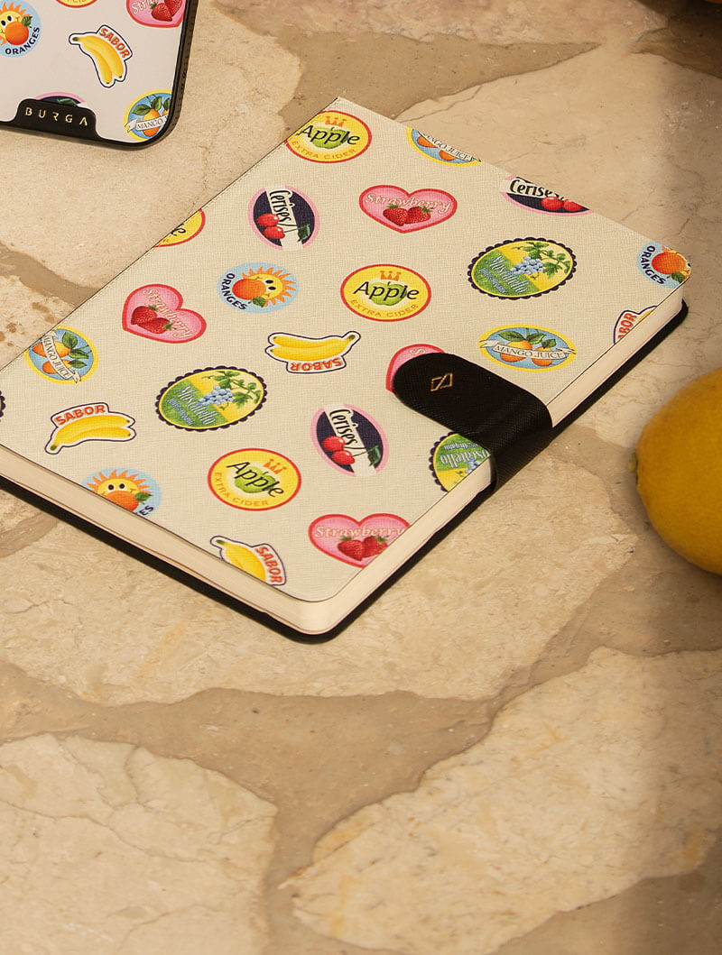 Notebook with colorful fruit stickers on a stone surface.