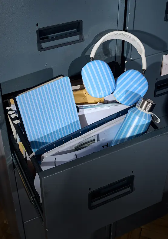 An open filing cabinet drawer containing files and a matching set of blue-striped headphones, notebook, and water bottle.