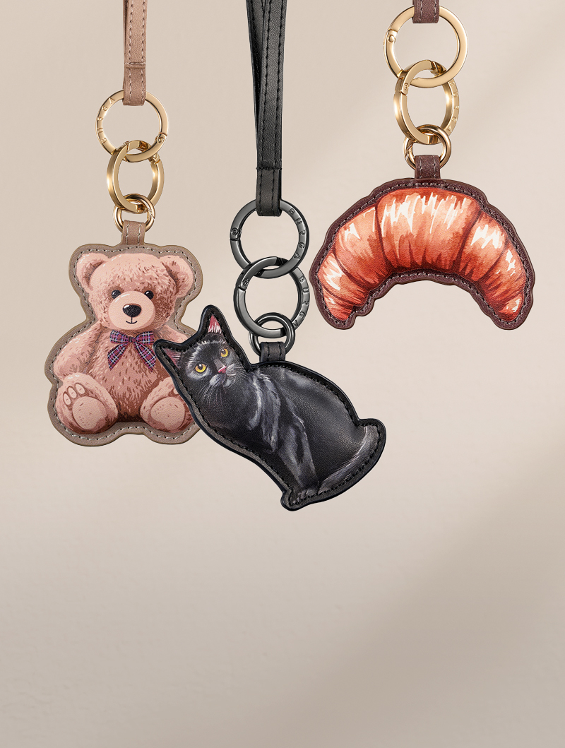 Three leather keychains hanging together: a teddy bear, a black cat, and a croissant.