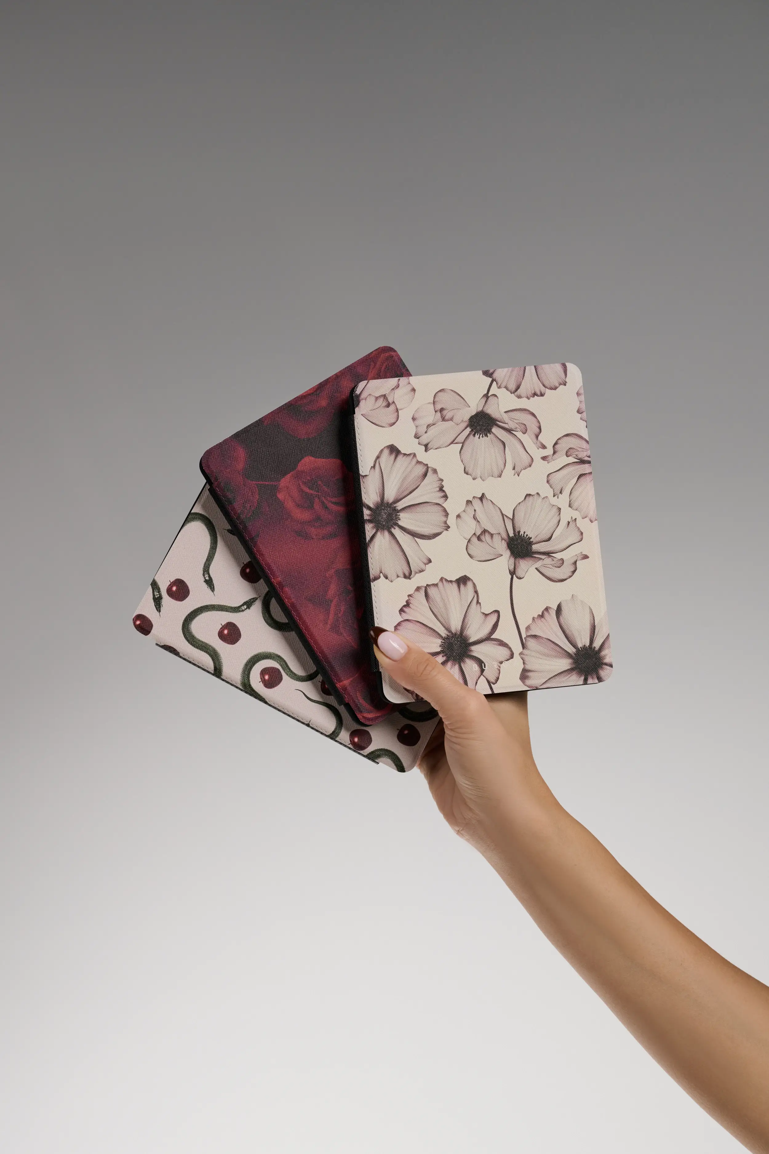 Hand holding three floral and patterned tablet covers.