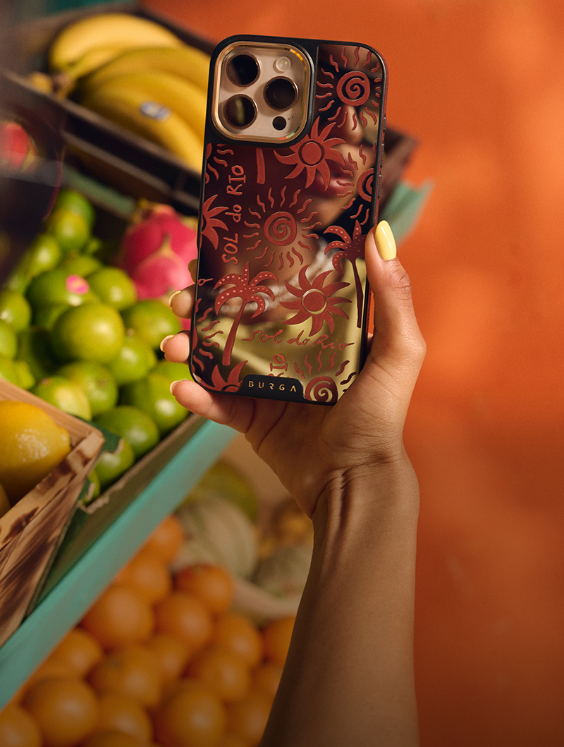 Hand holding a phone with a decorative case near fruit display.