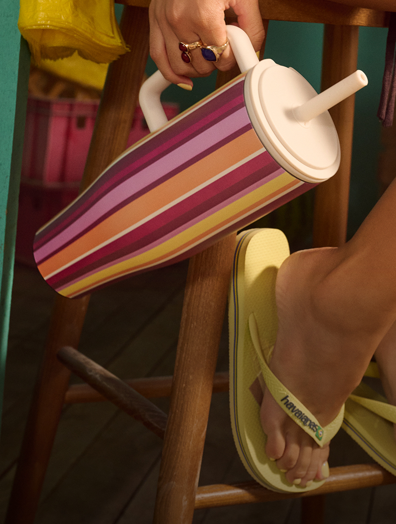 Person holding a striped tumbler with a straw, wearing yellow flip-flops.