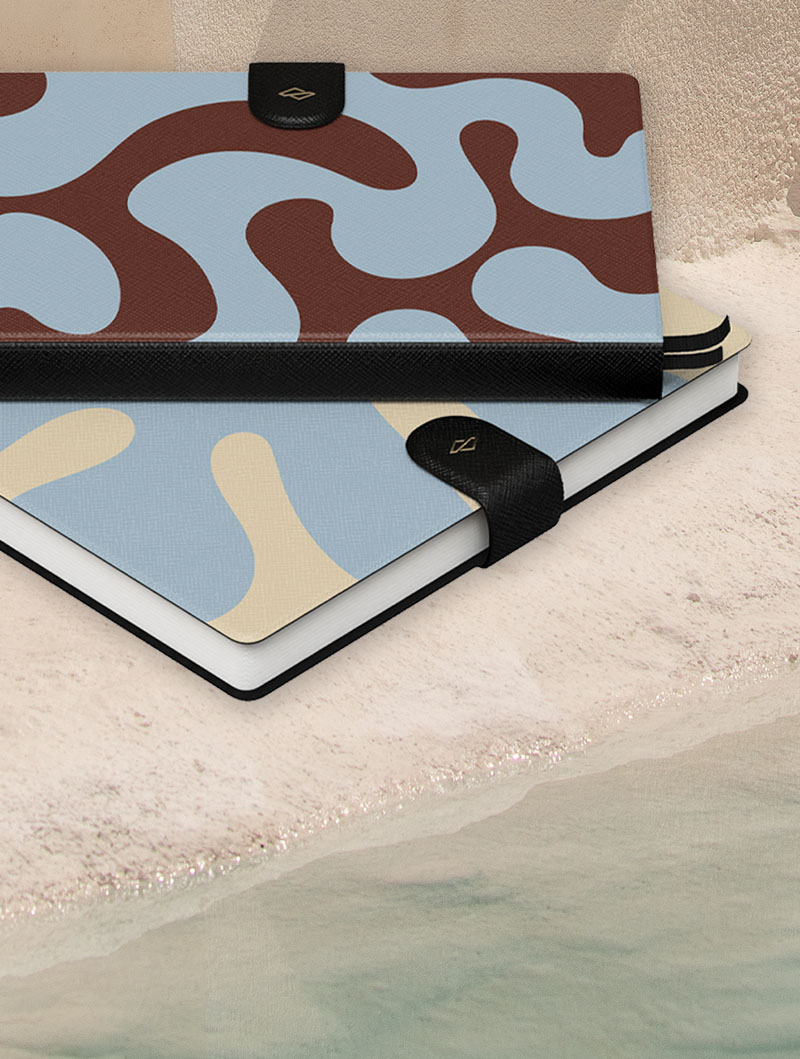 Two notebooks with abstract patterns on a sandy surface.