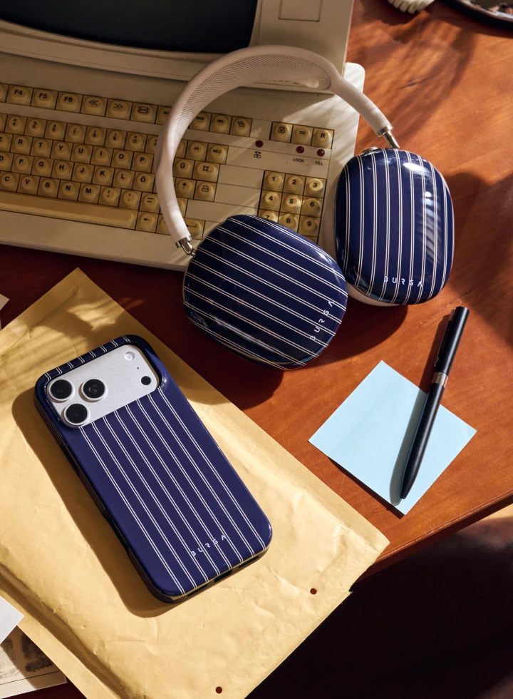 A pair of blue pinstriped headphones and a matching phone case on a wooden desk with a keyboard.