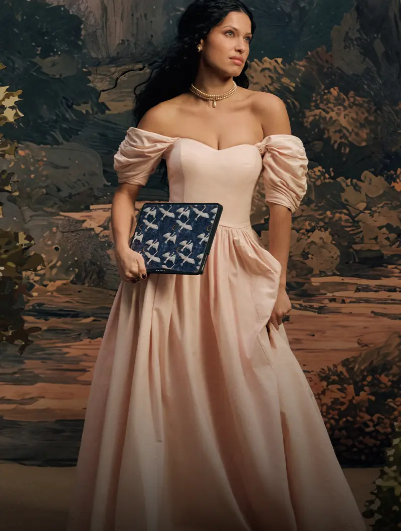A woman in a pink off-the-shoulder gown holding a tablet with a bird-patterned case.
