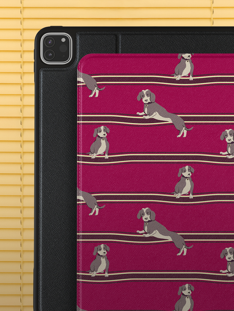 iPad with red case featuring a dachshund pattern, against yellow blinds.