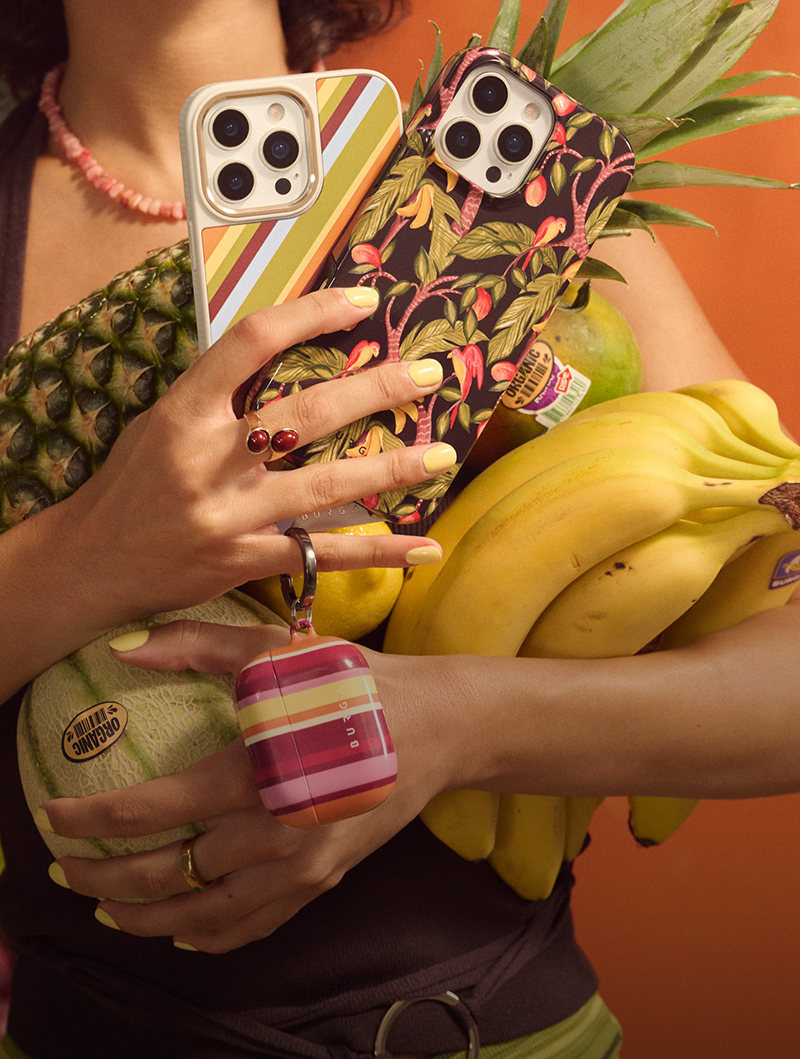 Person holding fruits and two phones with colorful cases.