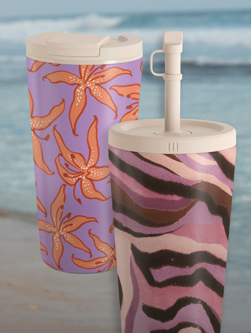 Two patterned travel mugs with floral and zebra designs on a beach background.