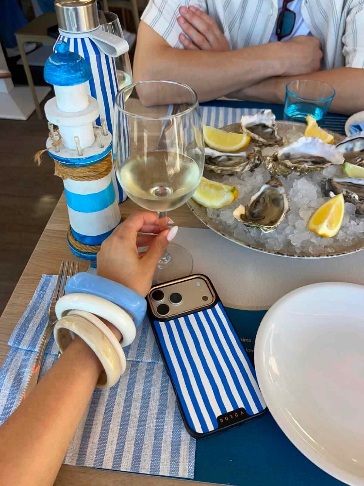 A table with a platter of oysters on ice, a glass of white wine, and nautical decorations.