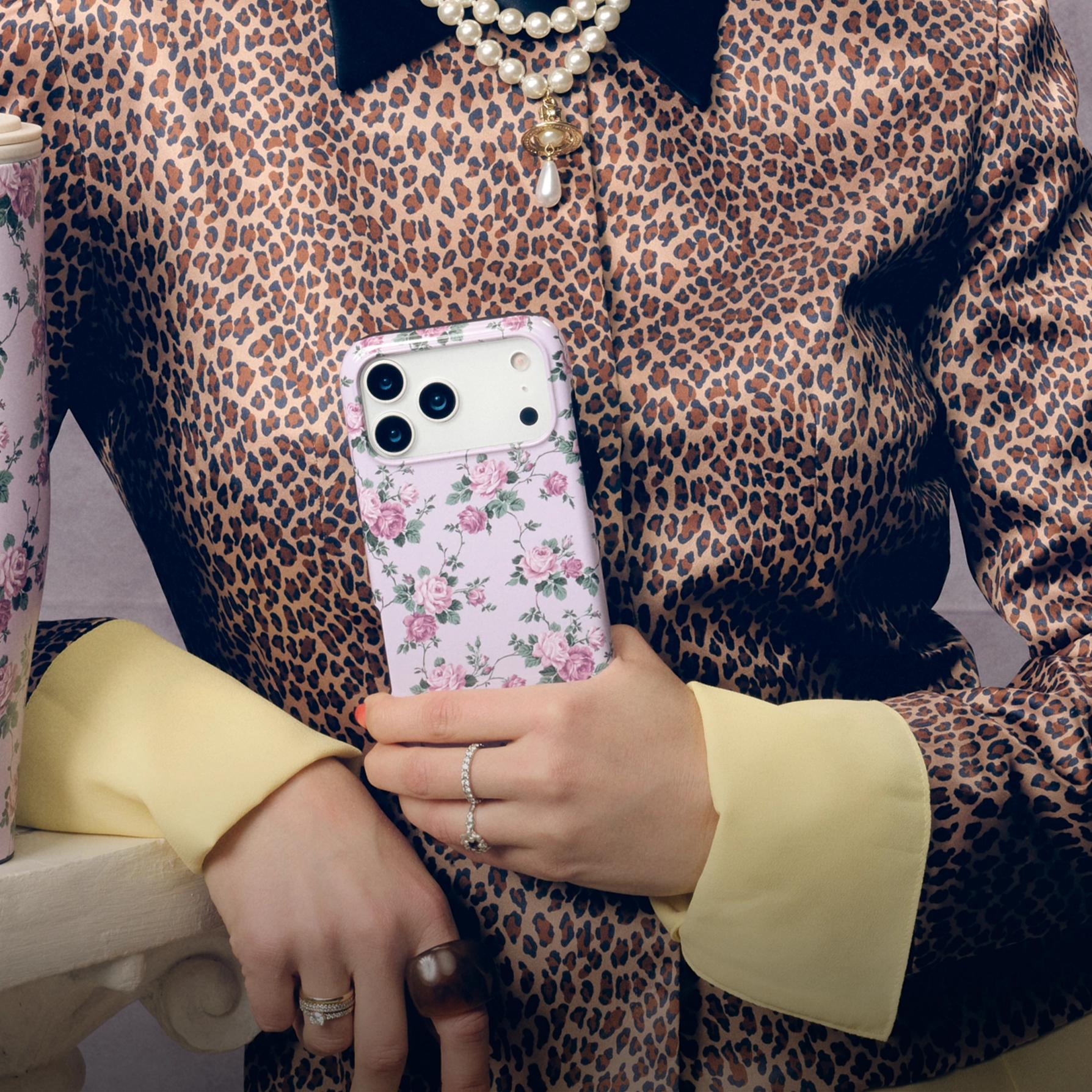 A person in a leopard-print jacket holds a phone in a light purple floral case.