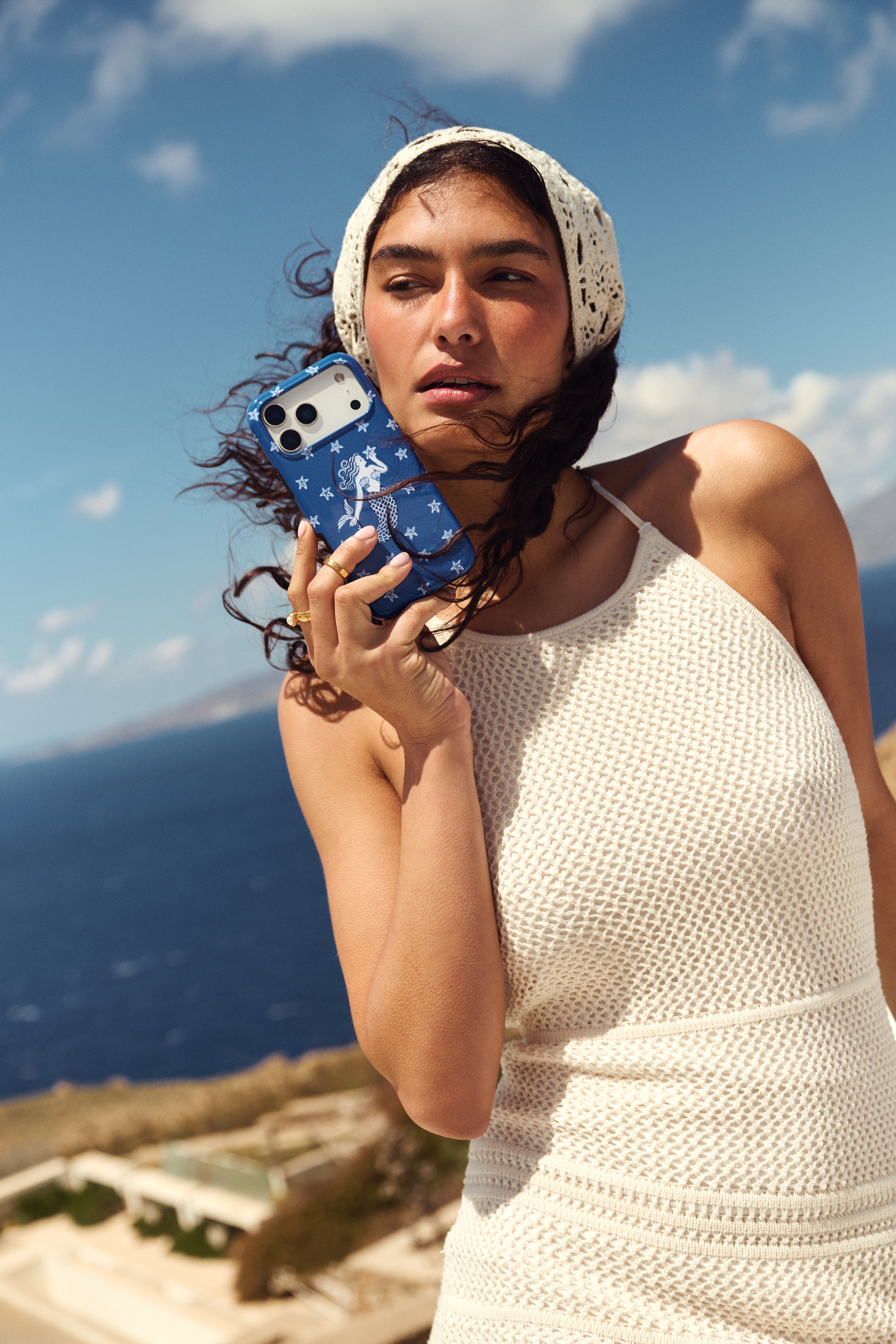 A woman in a white headscarf and knit top holds a blue phone case with a mermaid design.