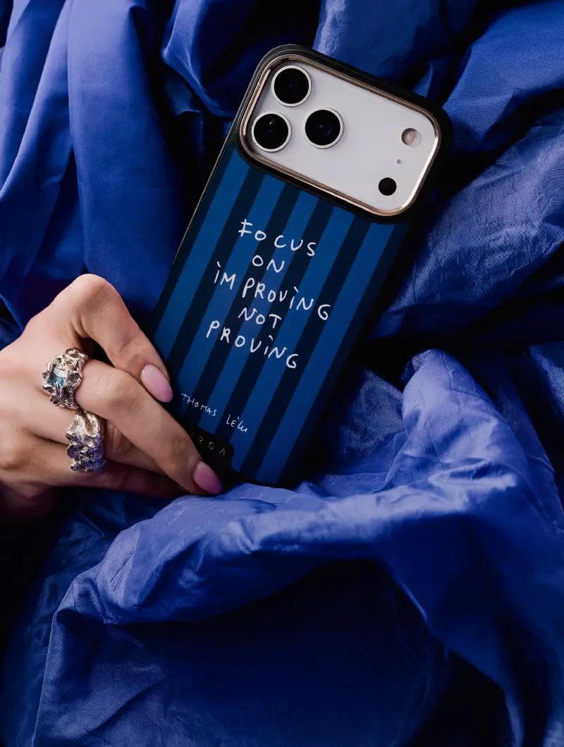 Hand holding phone with striped case saying, 'Focus on improving, not proving.'