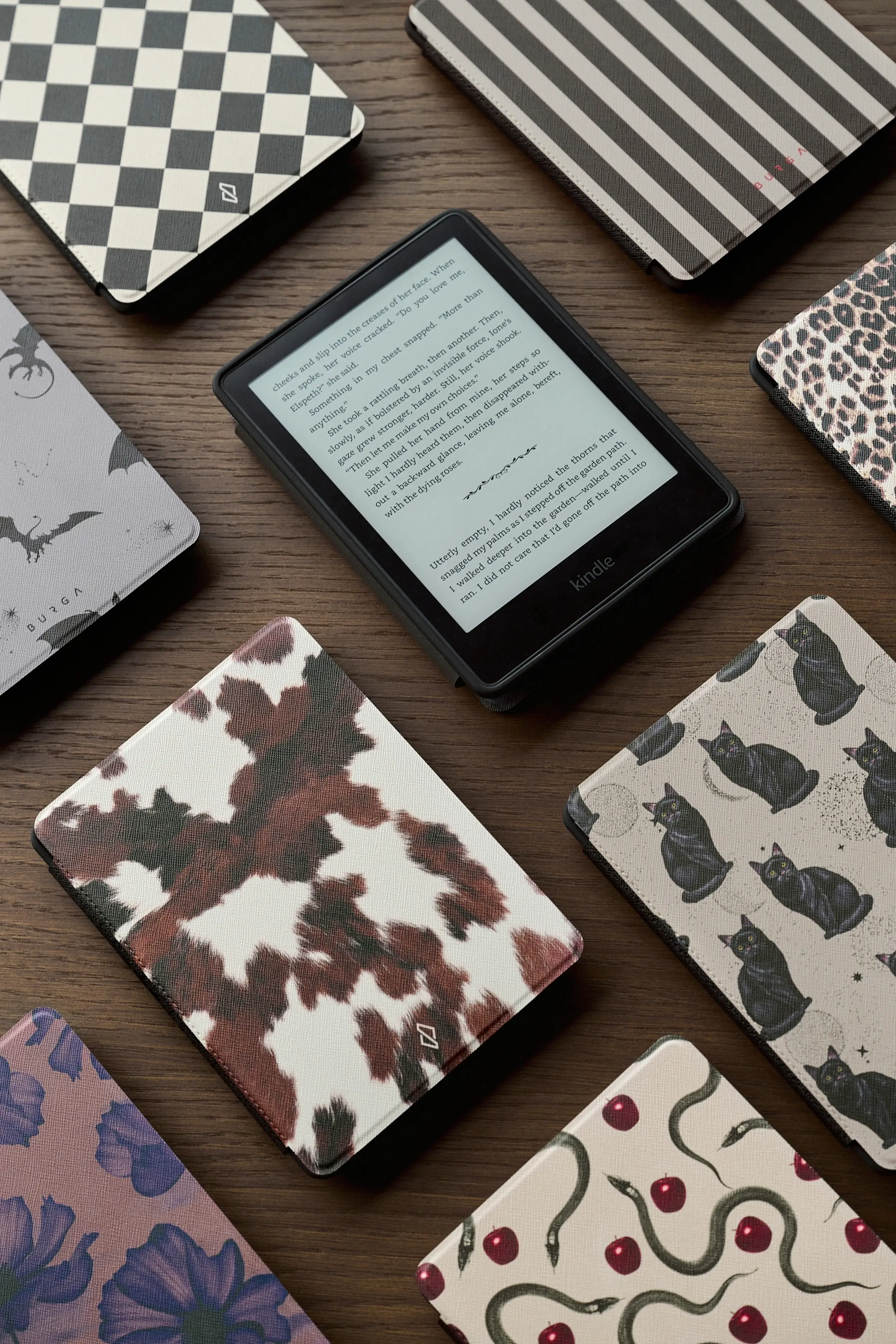 E-reader surrounded by various patterned covers on a wooden surface.
