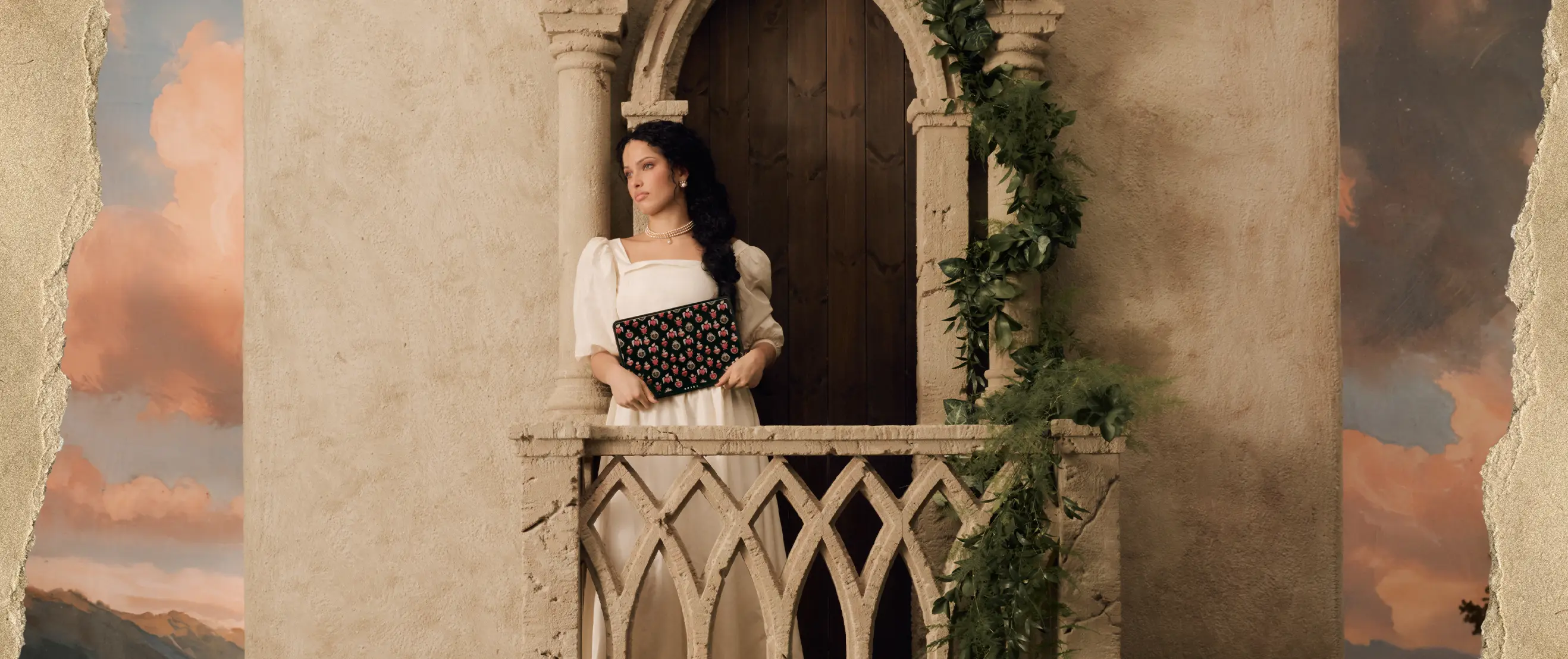 A woman in a white dress stands on a stone balcony, holding a black patterned clutch.