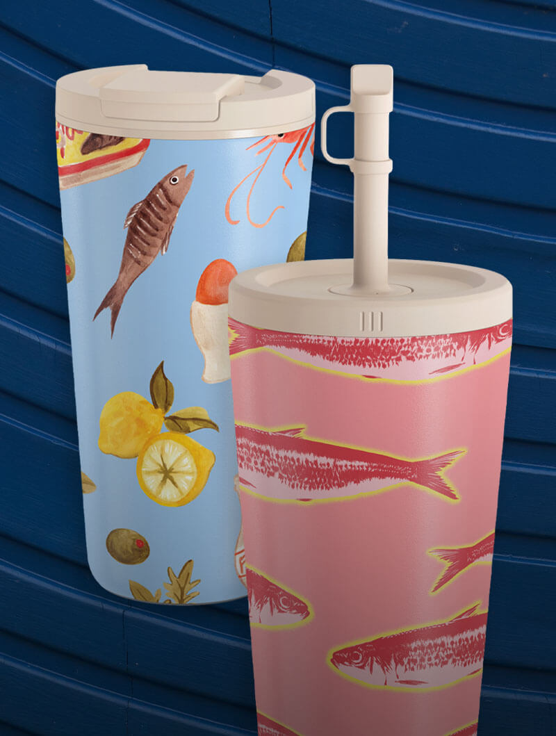 Two colorful travel mugs with fish and food patterns against a blue background.