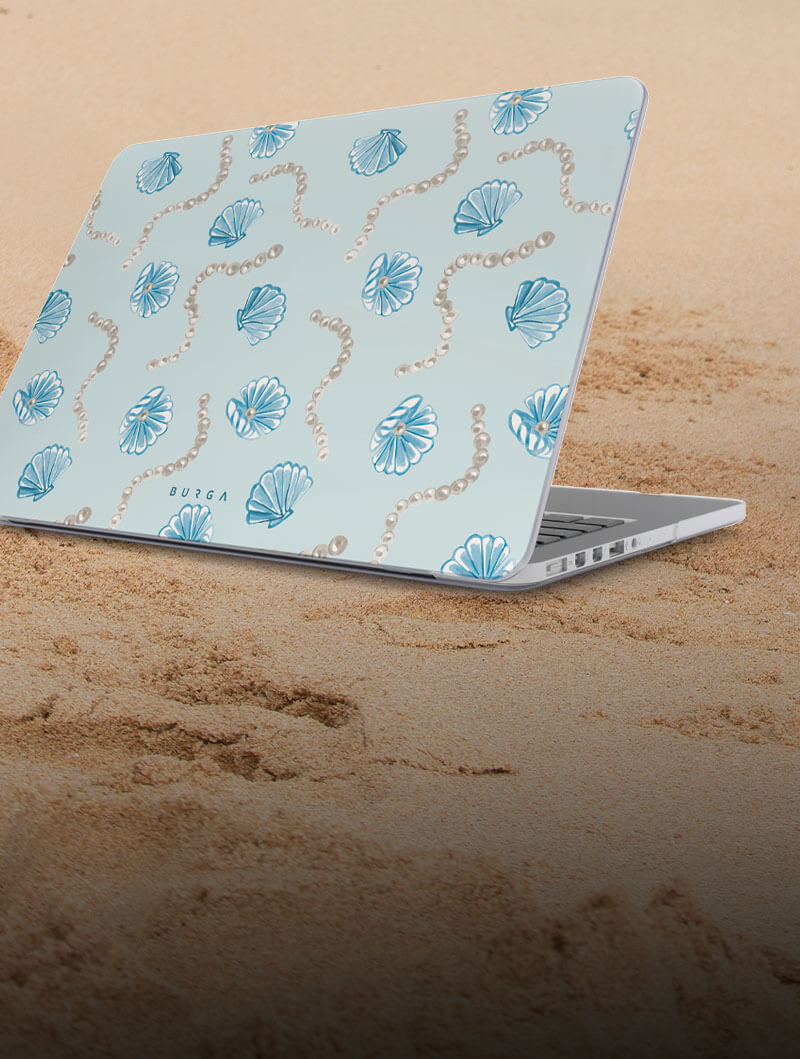Laptop with seashell design on sandy surface.