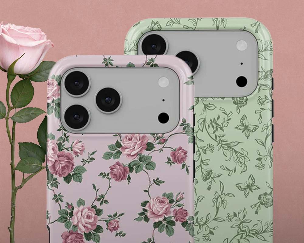 Two floral phone cases, one pink with roses and one green with vines, next to a pink rose.