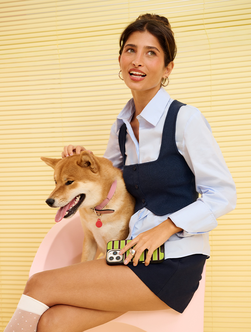 Person sitting with a dog, holding a smartphone, against a yellow background.