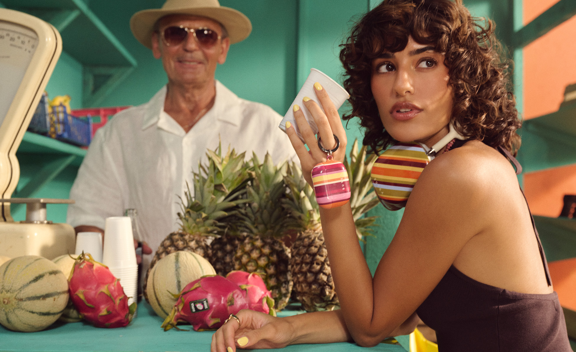 Woman holding a cup at a fruit stand with pineapples and melons.