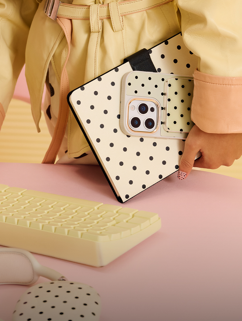 Person holding polka dot notebook next to yellow keyboard on a pink surface.