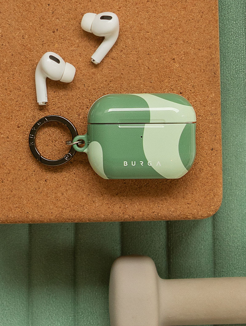 Green AirPods case with keyring and white earbuds on a cork surface.