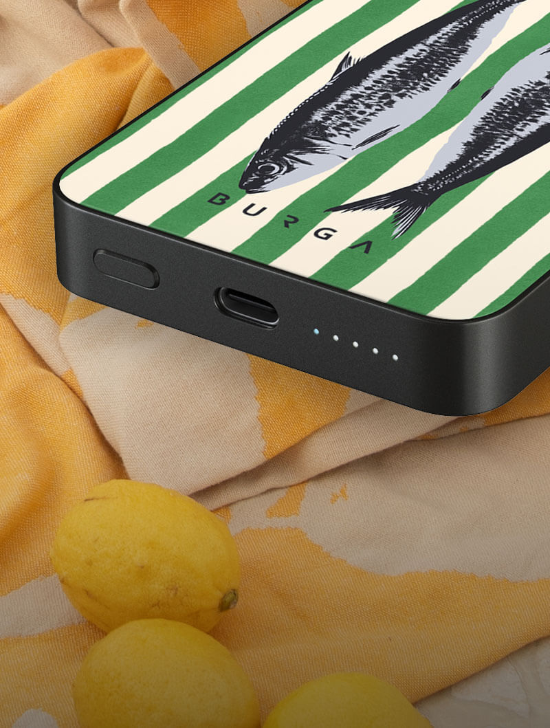 Power bank with fish design on striped background, placed on fabric with lemons.