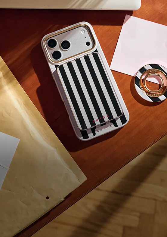 A phone in a black and white striped case sits next to a matching ring holder on a desk.