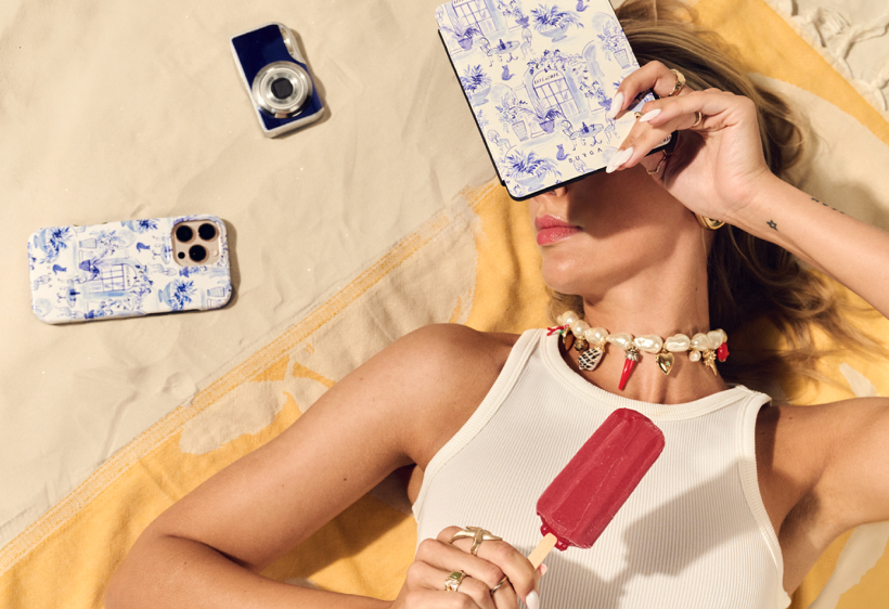 An overhead shot of a woman on a blanket holding a popsicle, with a phone and camera nearby.