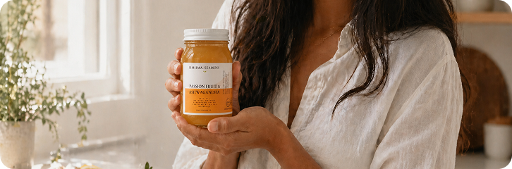 A person in a white linen shirt holds up a glass jar of Passion Fruit & Ashwagandha sea moss.