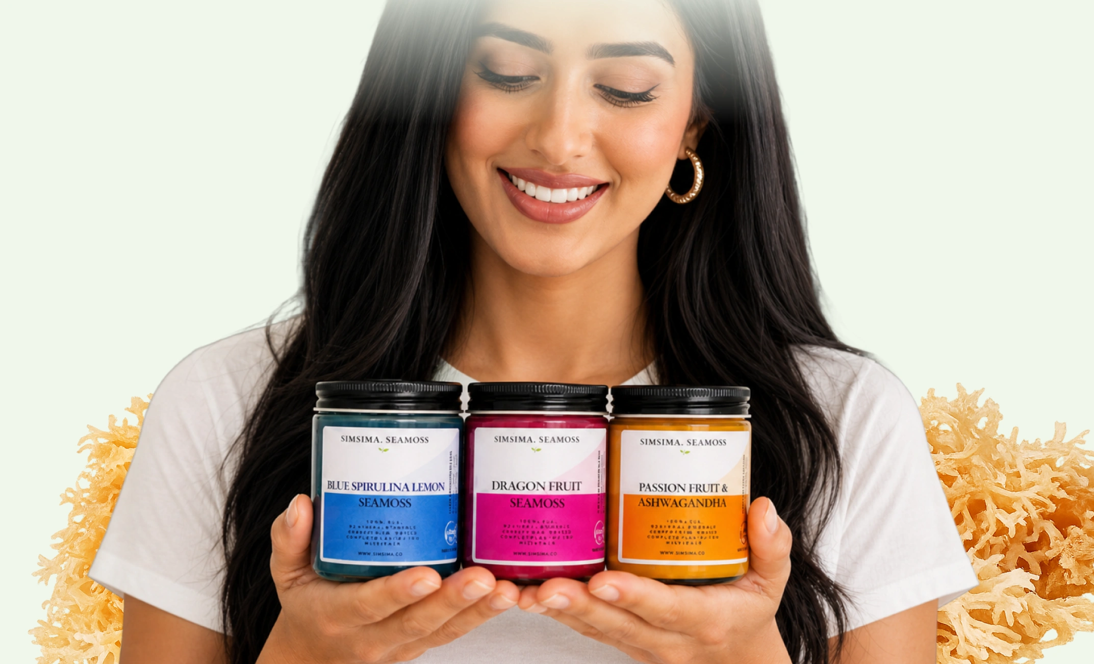 A smiling woman holds three jars of colorful Simsima Seamoss products in her hands.