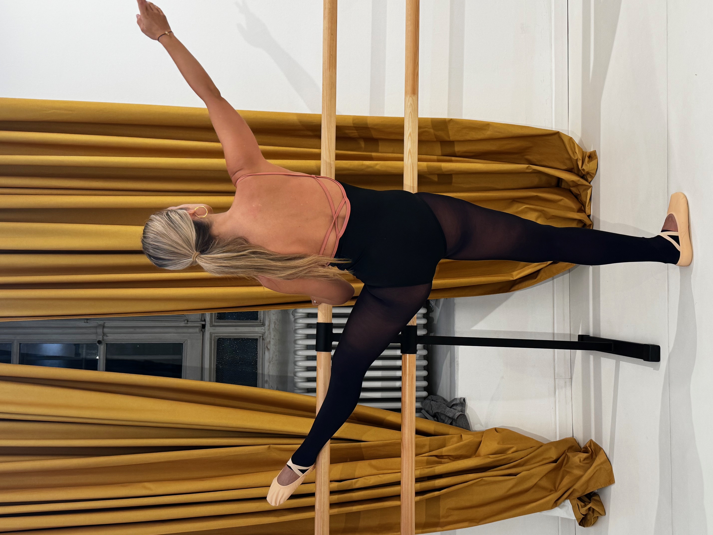Ballet dancer practicing at a barre in front of gold curtains.