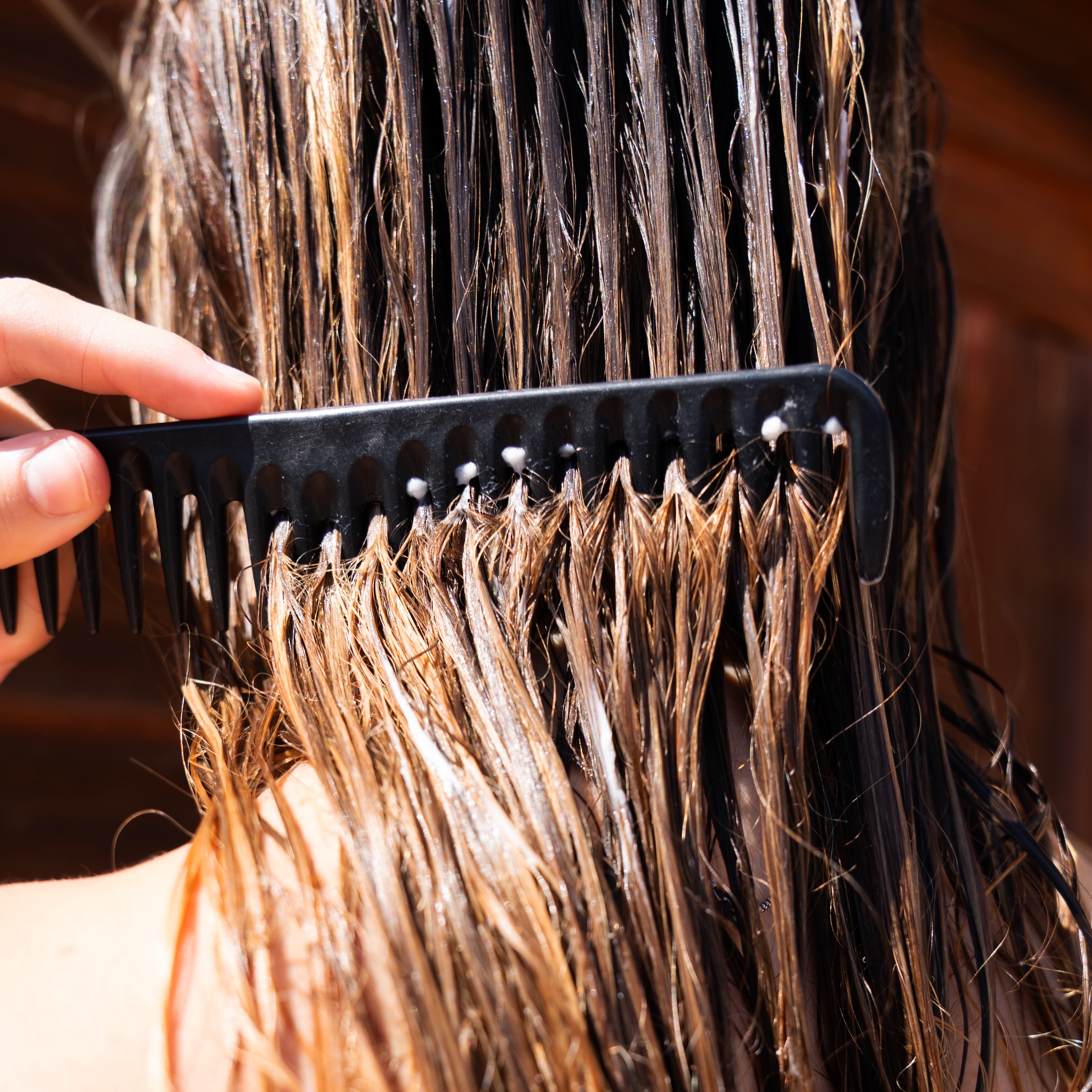 Dettaglio di una mano che pettina capelli bagnati e trattati con un pettine a denti larghi. L'immagine suggerisce l'efficacia della formula balsamo Originae, ideale per districare capelli secchi e sfibrati, rendendoli più gestibili.