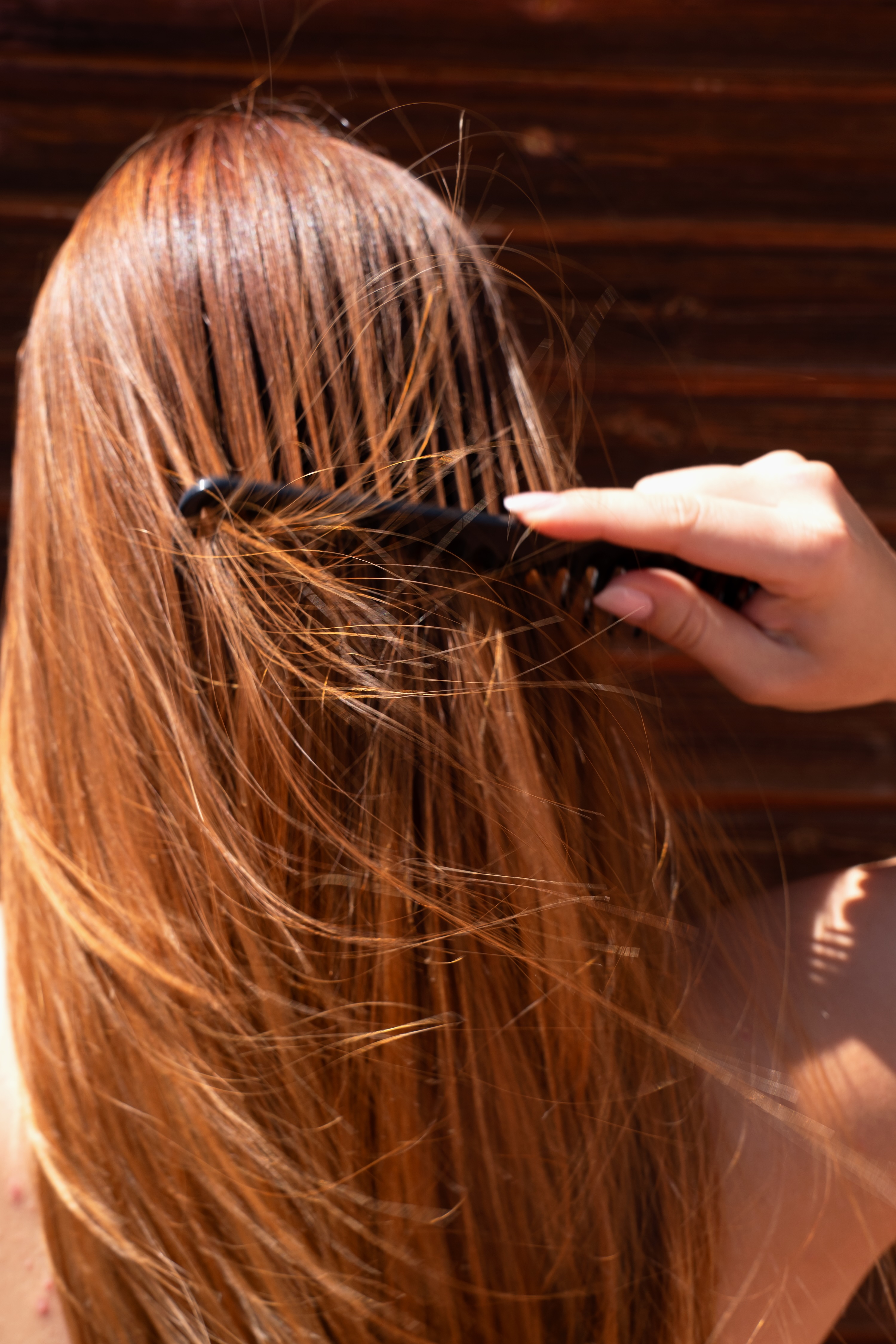 Dettaglio di lunghi capelli lisci e lucidi che vengono pettinati con cura, rappresentando l'efficacia dei prodotti Originae che proteggono dal sole e nutrono in profondità sia i capelli che il cuoio capelluto.