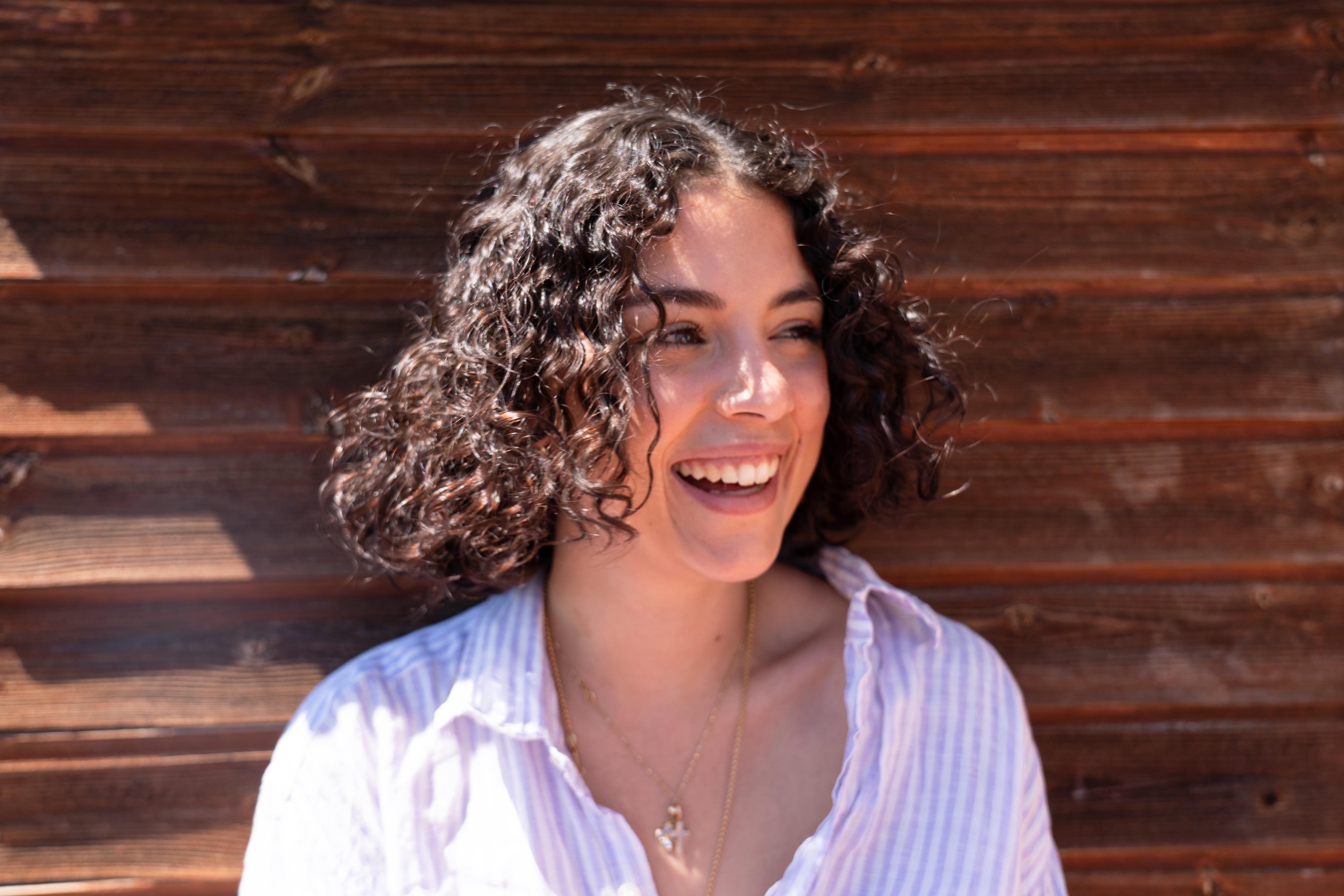 Ritratto di una donna sorridente con capelli ricci voluminosi e ben idratati, che irradia felicità e leggerezza. L'immagine rappresenta l'efficacia della routine per capelli ricci di Originae, formulata senza siliconi né ingredienti dannosi per un risultato naturale e sano.