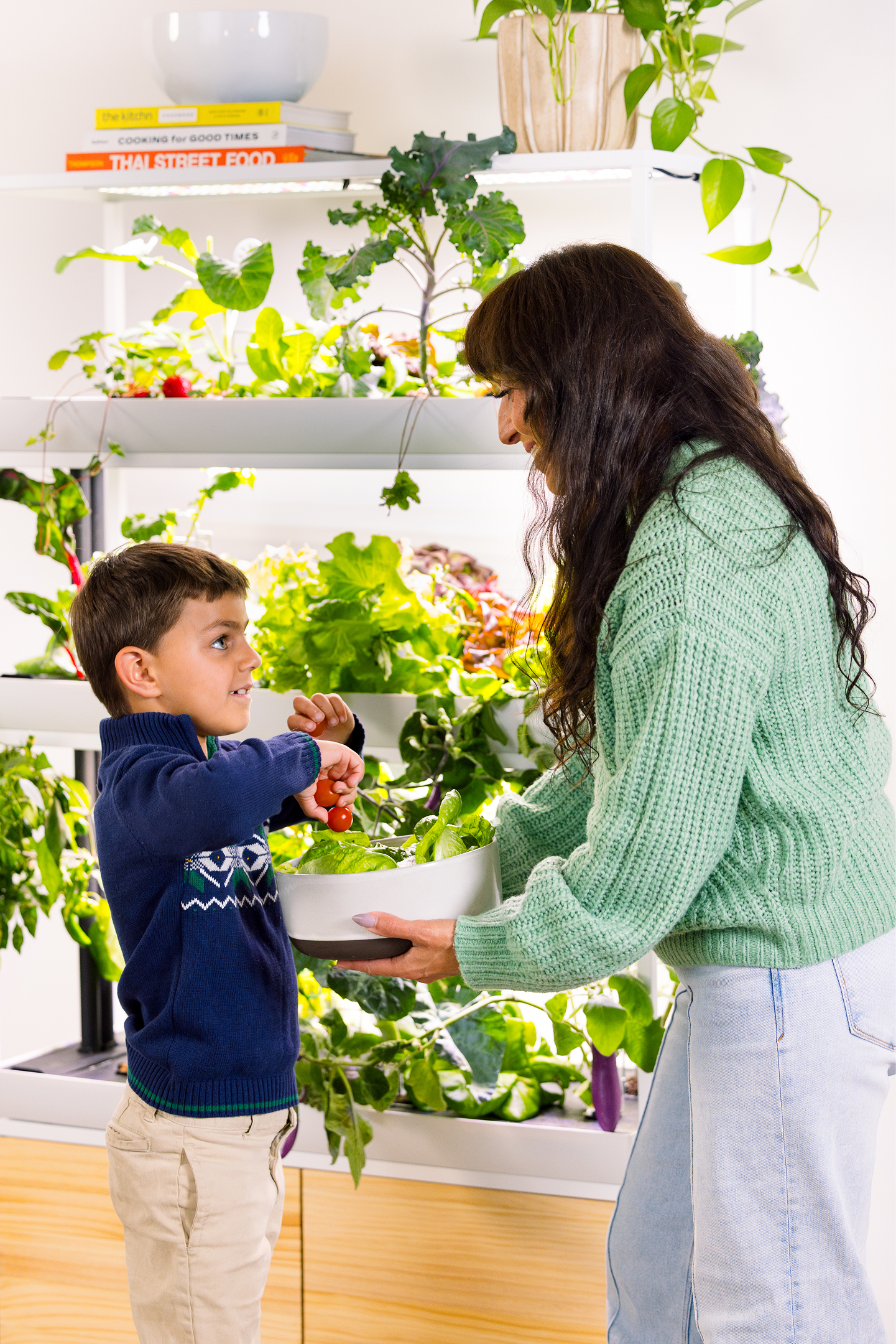 A woman and child harvesting vegetables from an indoor garden.