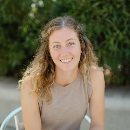 Person with long curly hair smiling outdoors.